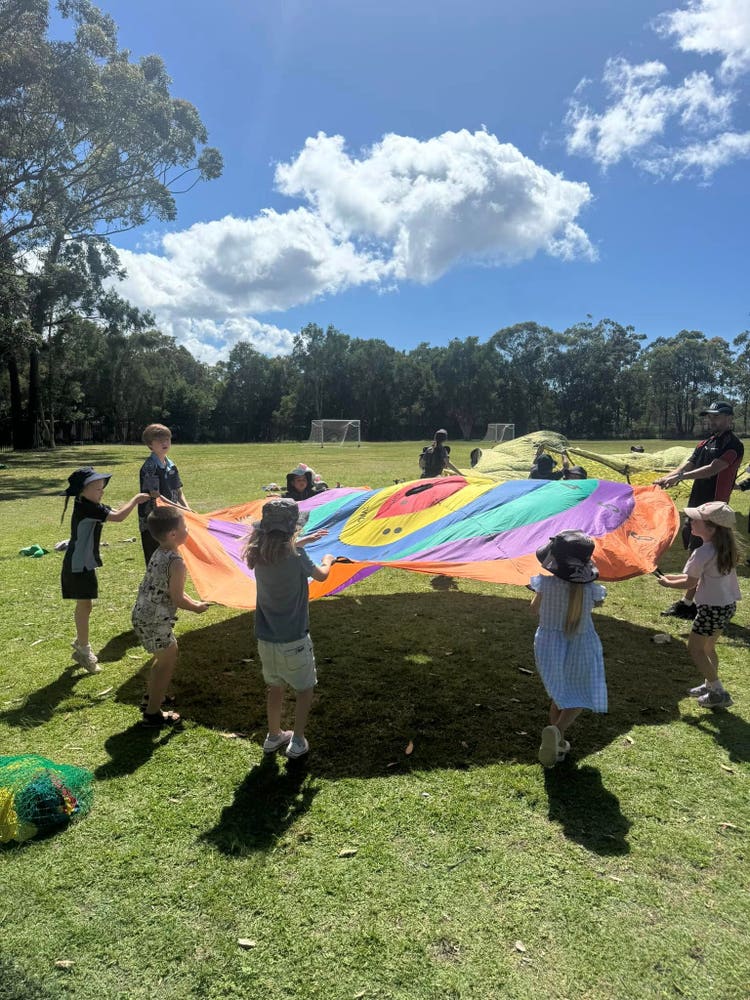 Students playing in the field with a parachute