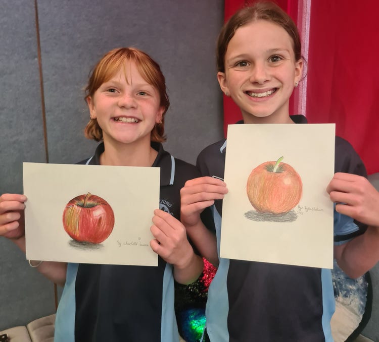 Two students with their still life drawings of red apples
